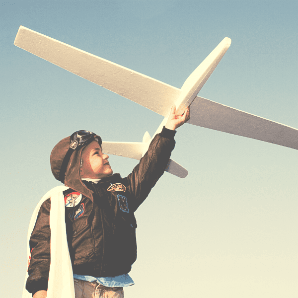 Nous observons un enfant habillé comme un pilote d'avion jouant avec un avion dans les airs, le tenant bras tendu. Cette image représente l'amélioration du pilotage grâce à la dématérialisation et qui est, en plus, un jeu d'enfants !